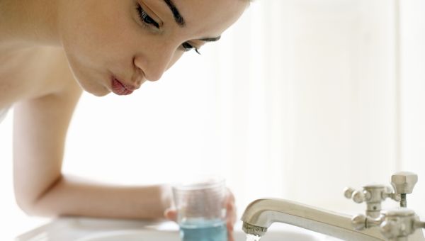 woman using mouthwash rinsing her mouth over the bathroom sink