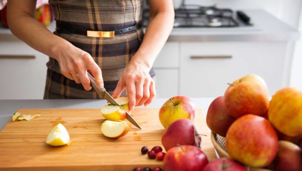 closeup of a woman wearing a tartan apron cutting apples on a cutting board in a kitchen