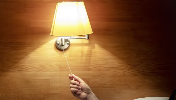 hand reaching to turn a light off next to bed
