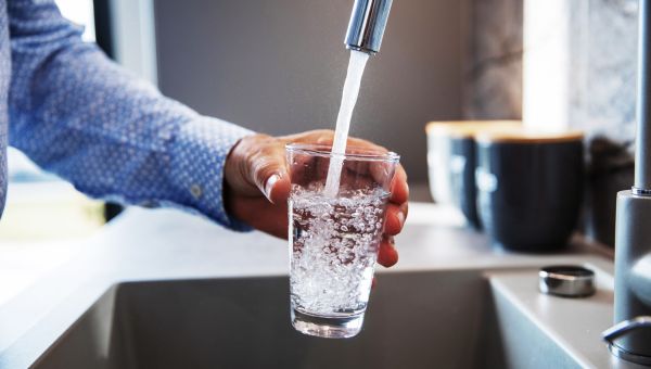 man using a kitchen faucet to fill a water glass
