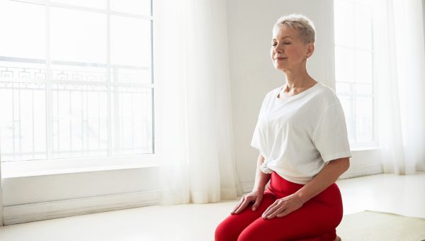 mature woman sitting on a mat at home doing meditation