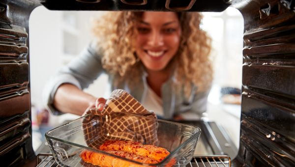happy woman pulling healthy dinner from oven