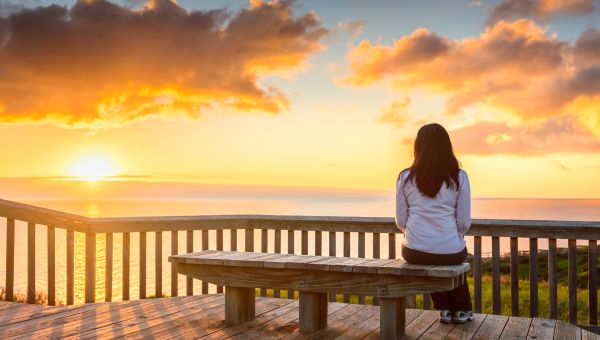 woman sitting alone on bench sunset