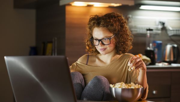 woman eating popcorn watching movie on laptop