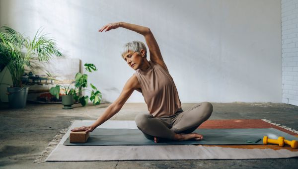 a middle aged white woman does a yoga pose on the floor to help improve flexibility and strengthen bones 