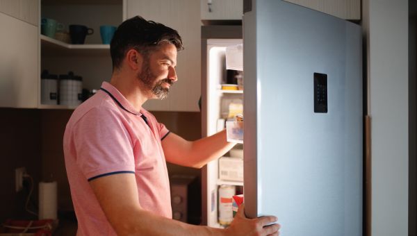 a white middle aged man with a beard stands in front of the refrigerator trying to decide what to eat before going to bed