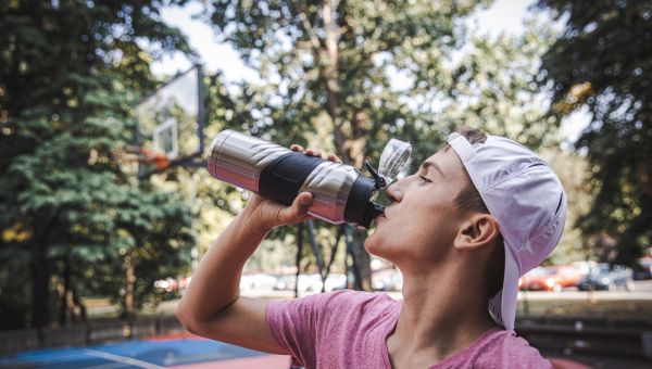 a young man drinks from a water bottle with a built-in filter after playing basketball on a basketball court outdoors