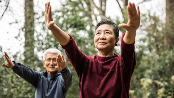 an elderly Asian American couple do a session of tai chi in a local park