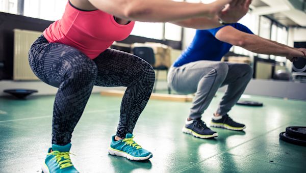 man and woman doing squats in gym