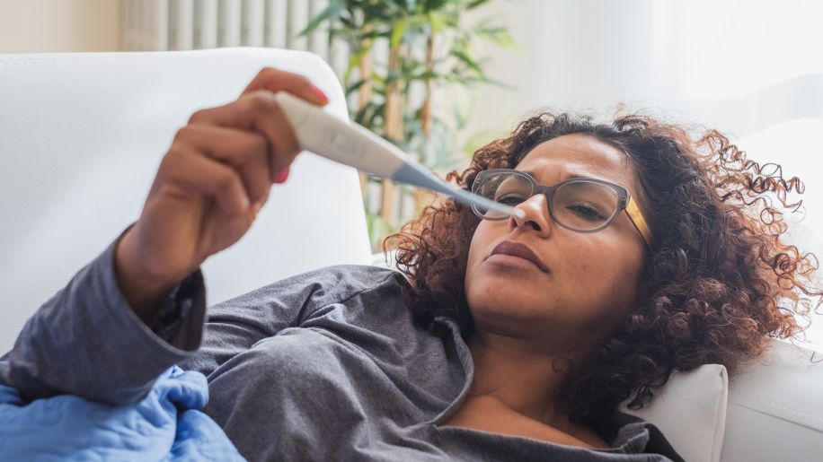 Sick black woman lying down checking thermometer