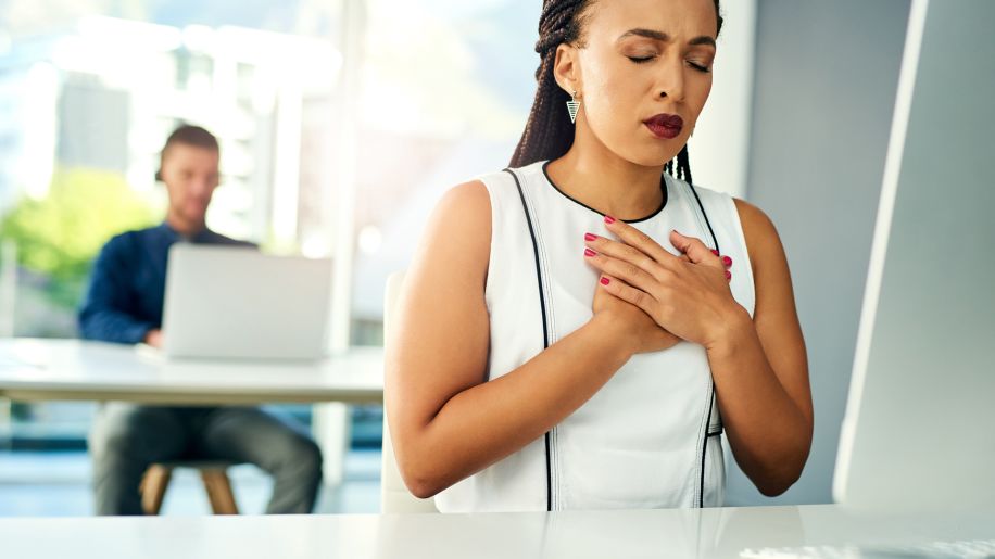 Woman closing her eyes and holding her chest at work.