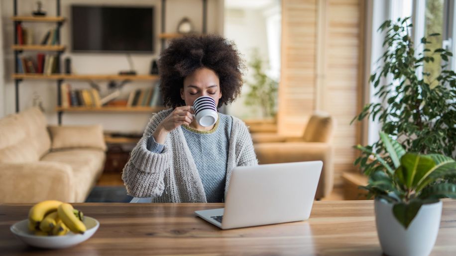 young woman enjoying a cup of coffee in front of her laptop
