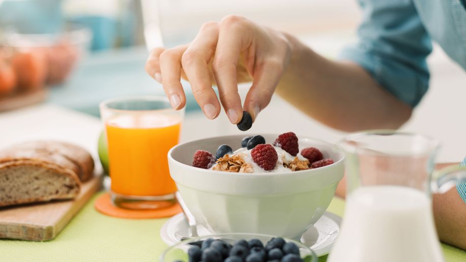 Woman delicately placing berries on top of her breakfast yogurt.