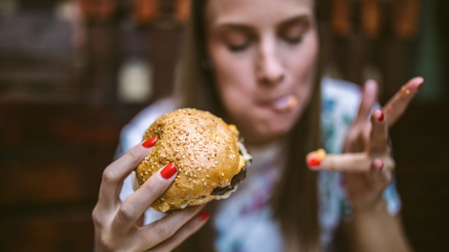 A woman eating a greasy cheeseburger.