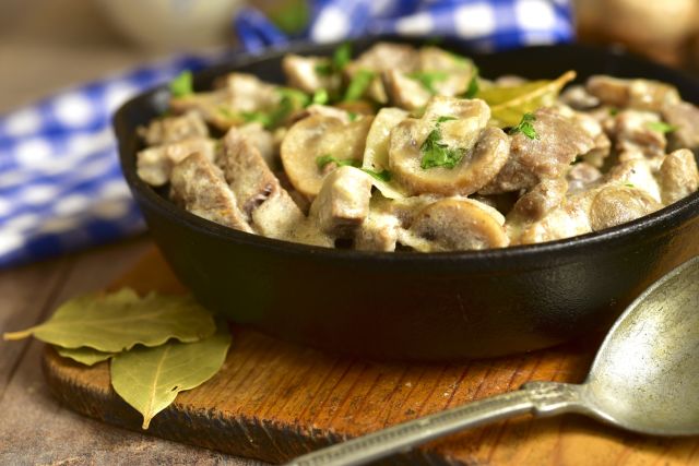 Beef stroganoff with mushrooms in a skillet pan on rustic background.