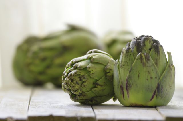 Some artichokes on a white wooden table in a rustic kitchen