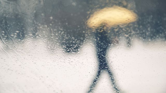 Through a rain-soaked window—a man walks by in the cold weather—suffering barometric pressure joint pain and arthritis. 