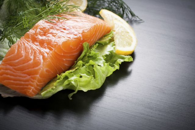 Delicious salmon fillet, rich in omega 3 oil, aromatic spices and lemon on fresh lettuce leaves on black wooden background. Healthy food, diet and cooking background with copy space.