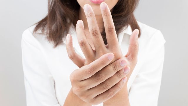 A woman holds her hand and wonders about rheumatoid arthritis (RA) causes and risk factors and whether RA is genetic.