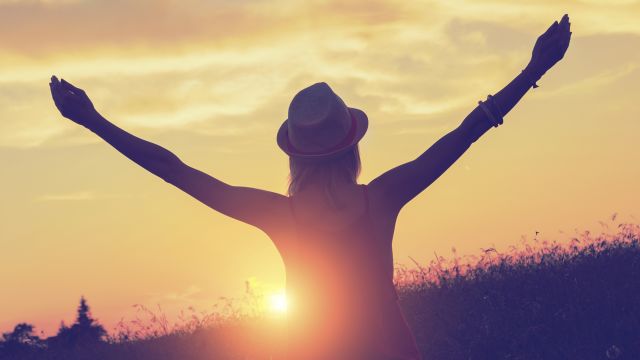 Woman raising arms in front of sunset