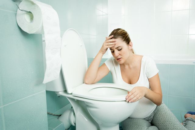 Pregnant young woman leaning on toilet and feeling sick