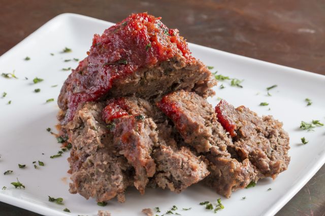 Sliced freshly cooked traditinal meatloaf with ketchup tomato sauce isolated on white plate