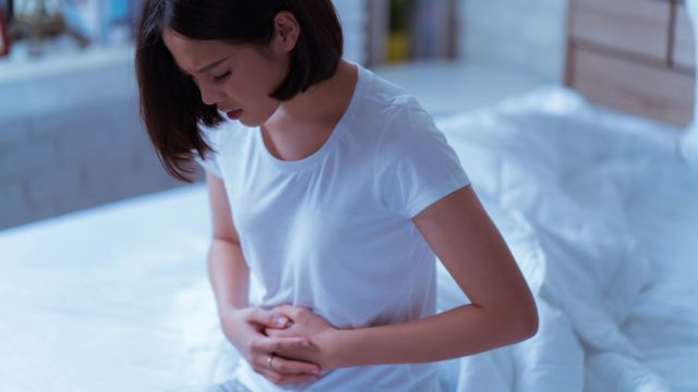 woman holding stomach, bedroom, bed