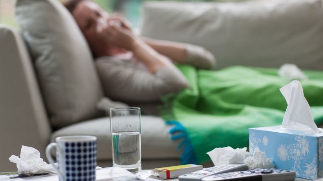 Sick woman laying on sofa blowing her nose