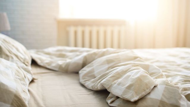 a bed with rumpled sheets lies bathed in bright morning sunlight