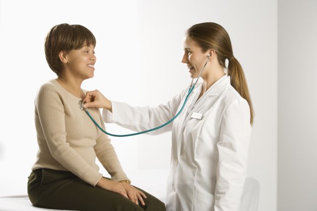 Caucasian mid-adult female doctor examining African American middle-aged female patient with stethoscope.