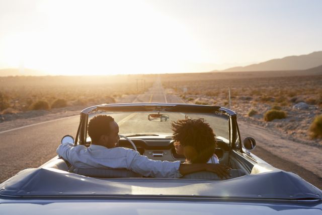 couple in convertible driving into sunset