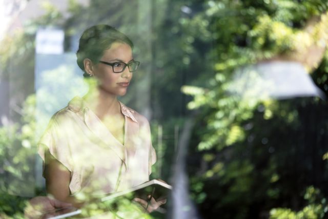 woman gazing out a window holding a device