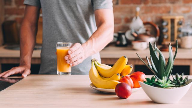 A man enjoys a glass of orange juice in his kitchen.