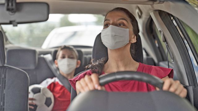 woman in masking driving child to soccer practice