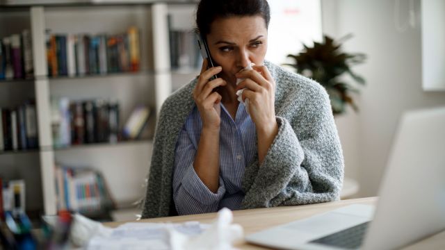 woman blowing nose in front of laptop