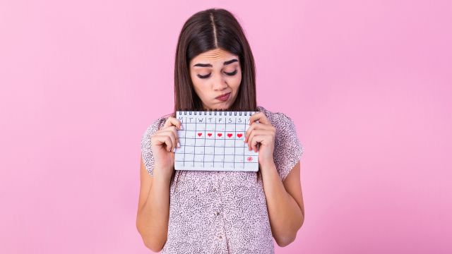 Young woman looking at a menstrual cycle calendar marked with hearts.