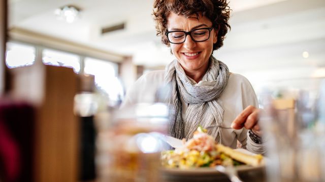A woman smiles, eating a healthy meal as part of her psoriatic arthritis diet, avoiding foods that trigger flareups.