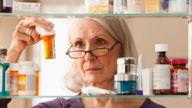 An older woman looks through the medications she takes to combat the long-term effects of shingles.