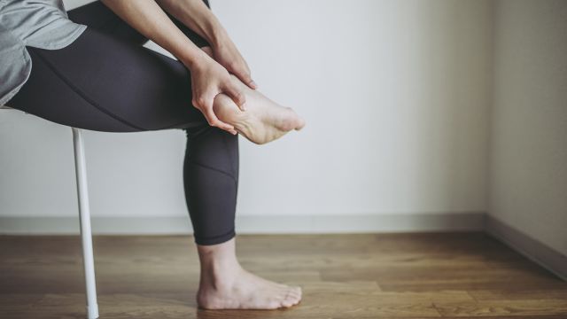 Woman rubs her aching feet while sitting on a chair. 