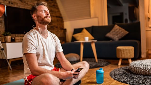 Man mediates in living room while listening to music on headphones. 