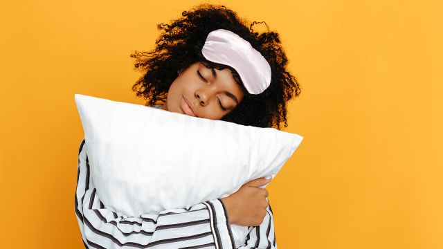 Young woman with sleep mask on her forehead holds and hugs a pillow.