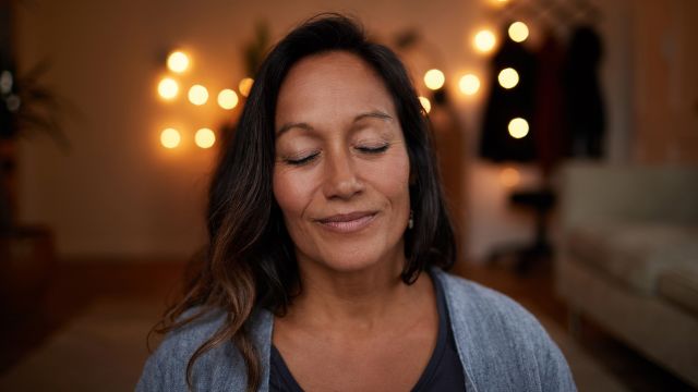 mature woman meditating and smiling in a dimly-lit room