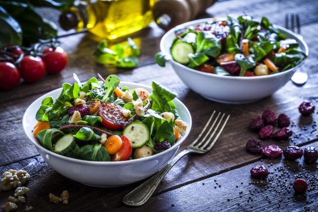 two fresh healthy looking salads in bowls on rough-hewn dining table