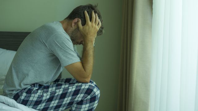 A stressed man sits on bed with head in hands.