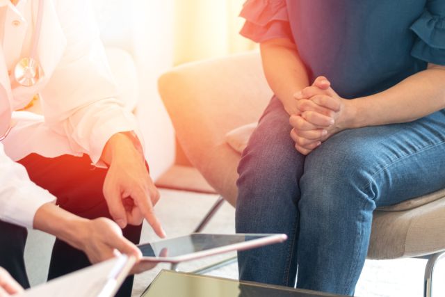 woman sits and discusses an issue with a healthcare provider, using an tablet computer