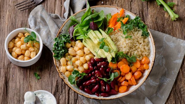 Bowl filled with spinach, romaine, chickpeas, carrots, quinoa, kidney beans and kale.