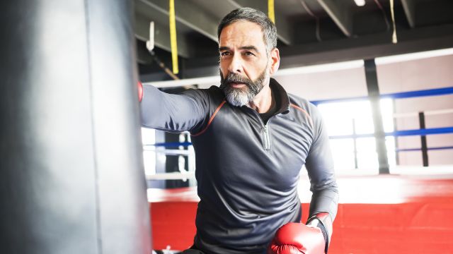 A middle-aged man punches a heavy bag for exercise.