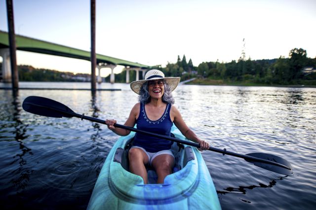 Middle aged woman smiling while paddling a kayak in late afternoon