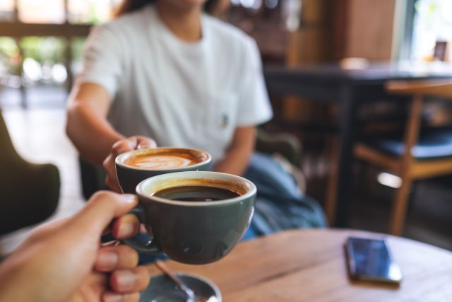 two people in a coffee shop hold out their mugs of coffee