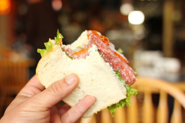 a hand holds up a salami sandwich on white bread